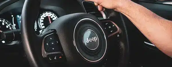 Close-up of a Jeep steering wheel and illuminated dashboard gauge cluster.