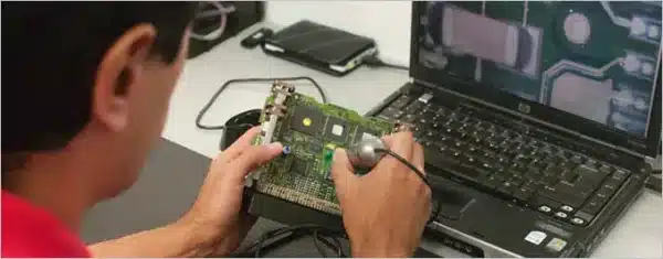 A technician using specialized equipment connected to a laptop to reprogram and flash a vehicle's Engine Control Module (ECM) circuit board.